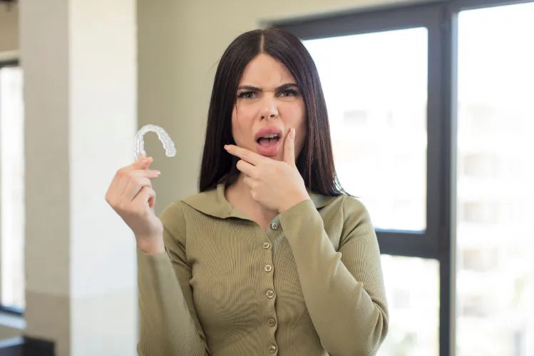 An image of a girl holding aligners with her mouth and eyes wide open and her hand on her chin.