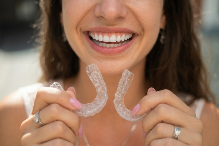 Smiling woman holding two clear mouth guards in front of her teeth